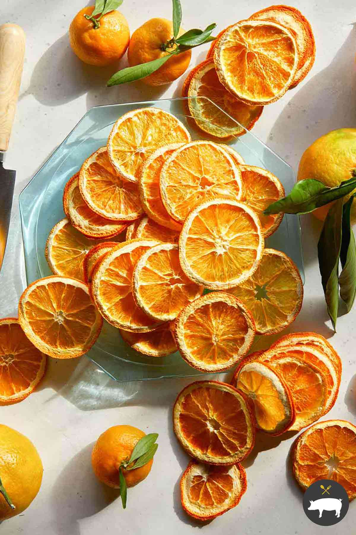 Dehydrated orange slices on a plate with some whole oranges next to it.
