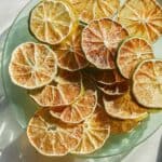 Dehydrated lime slices on a plate next to a fresh lime.