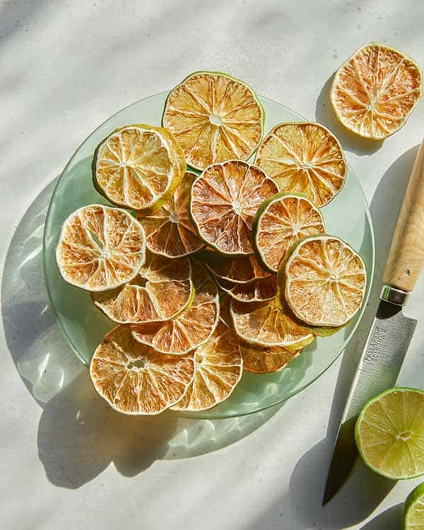 Dehydrated lime slices on a plate next to a fresh lime. 