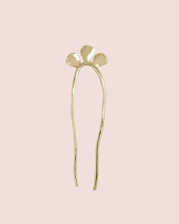 A brass hair pin on a pink background. 