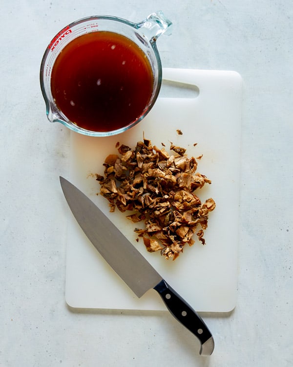 Dried mushrooms being chopped with broth next to it.