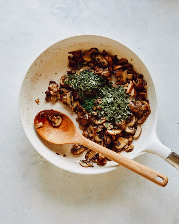 Herbs and mushrooms sauted in a skillet.