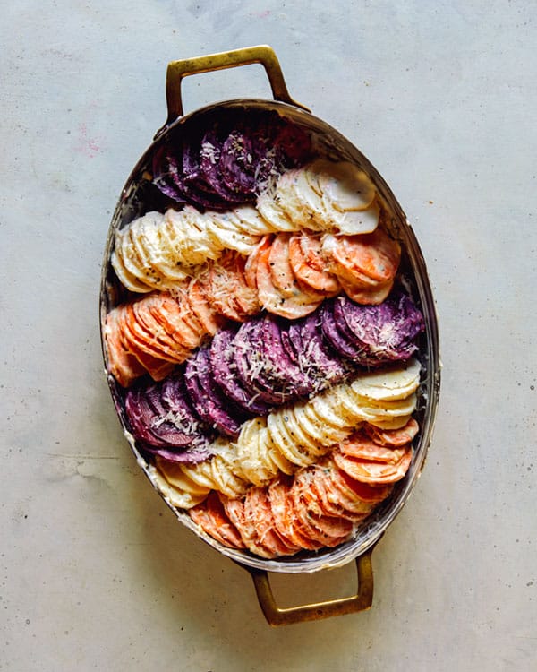 A baking dish full of sliced root vegetables to make a root vegetable gratin.
