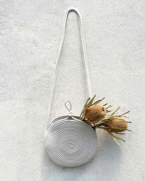 A purse made out of rope with  flowers in it hanging on a wall. 