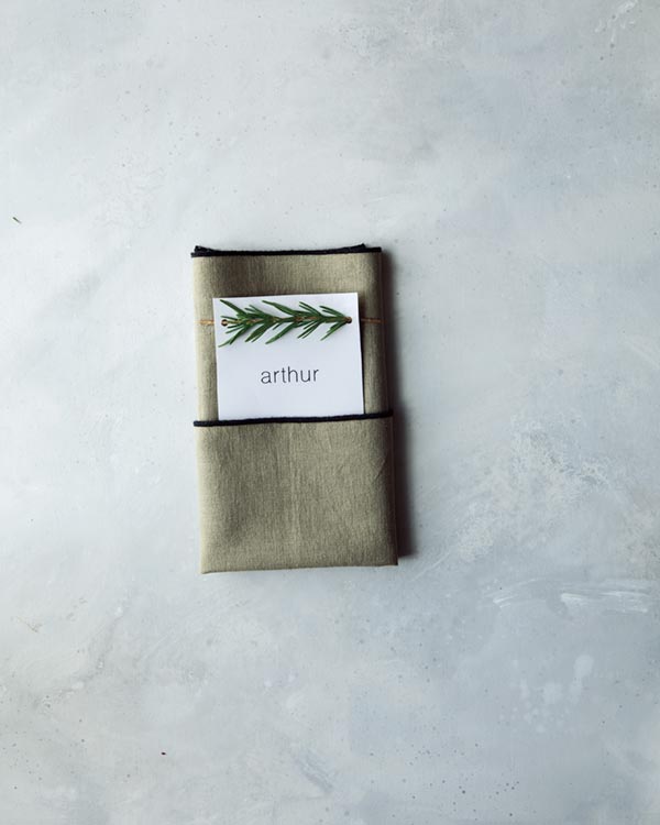 Folding a napkin to create a pocket for rosemary sprig place cards.