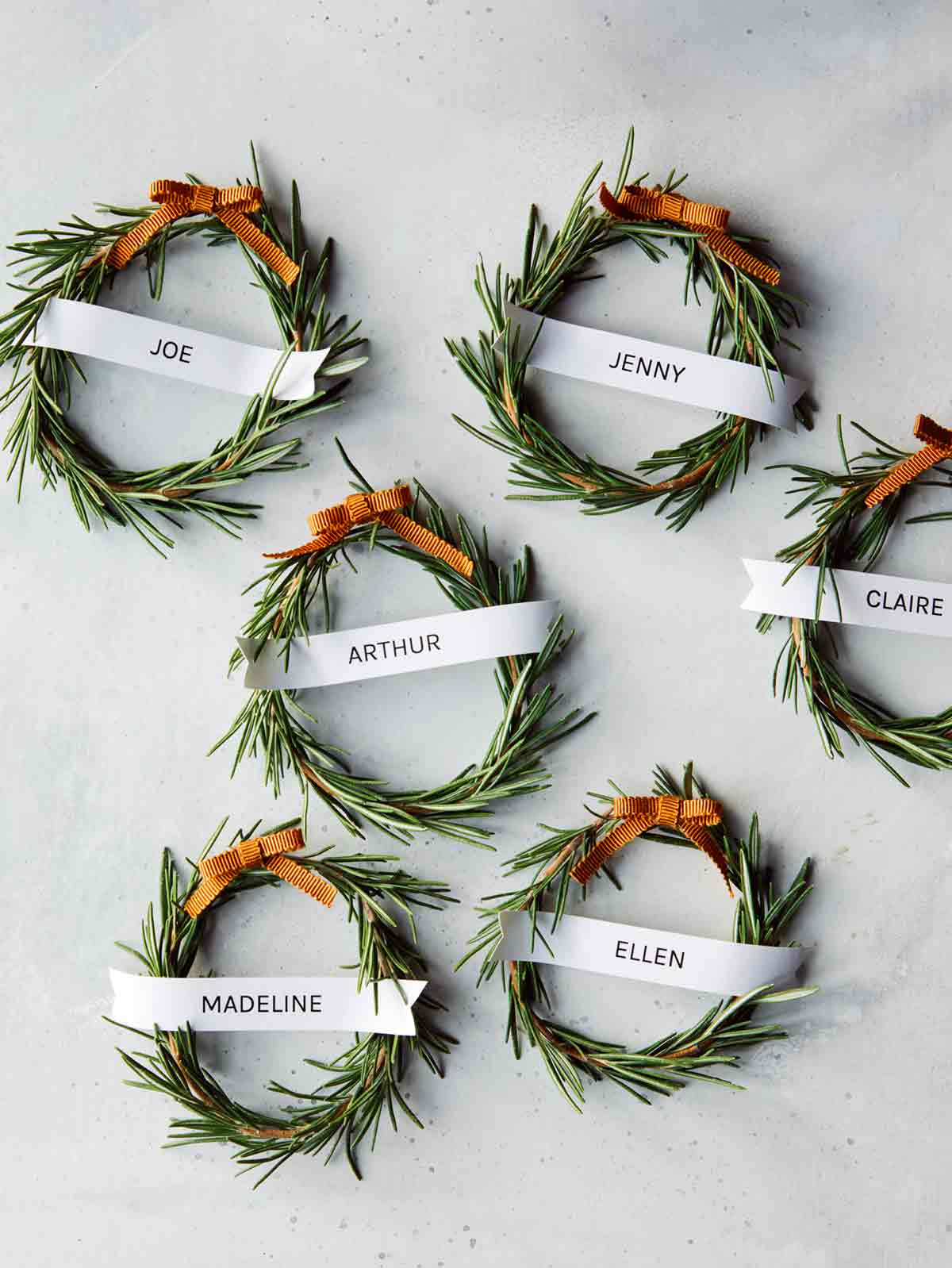Six rosemary wreath place cards on a table spread out. 