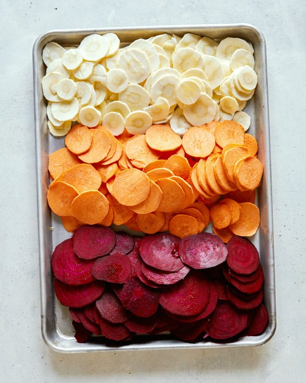 A baking sheet with sliced root vegetables on it.