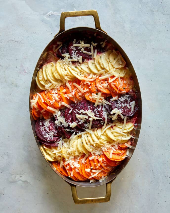 Root vegetable gratin with shredded cheese on top ready to go back into the oven.