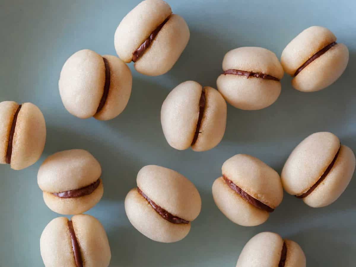 A close up of a bunch of baci di dama on a light blue surface.