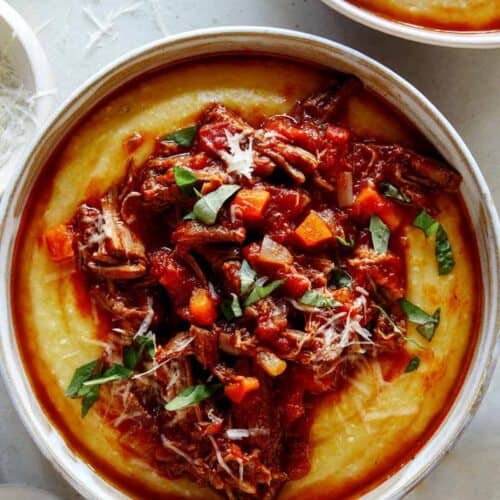 Beef ragu in a bowl with polenta and pepper on the side.