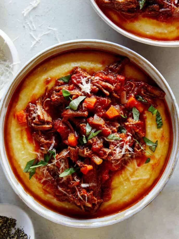 Beef ragu in a bowl with polenta and pepper on the side.