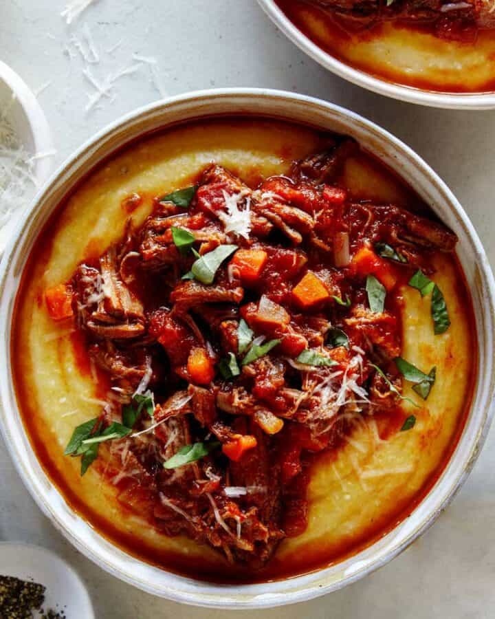 Beef ragu in a bowl with polenta and pepper on the side.