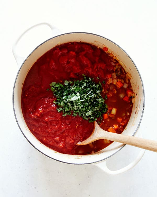 Veg with broth and tomatoes with herbs in a stock pot.