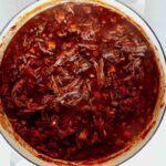 Braised beef shredded in a stock pot.