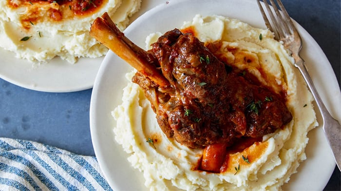 Braised lamb shanks over mashed potatoes on a plate.