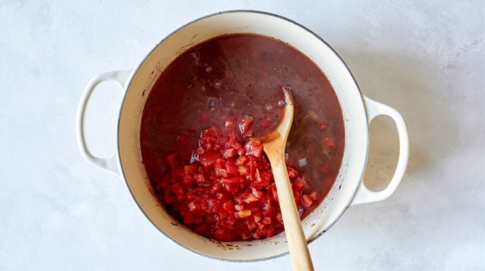 Tomatoes and stock in a pot to make braised lamb shanks.