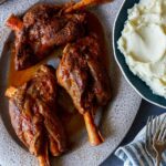 Braised Lamb shanks on a platter with mashed potatoes next to it.