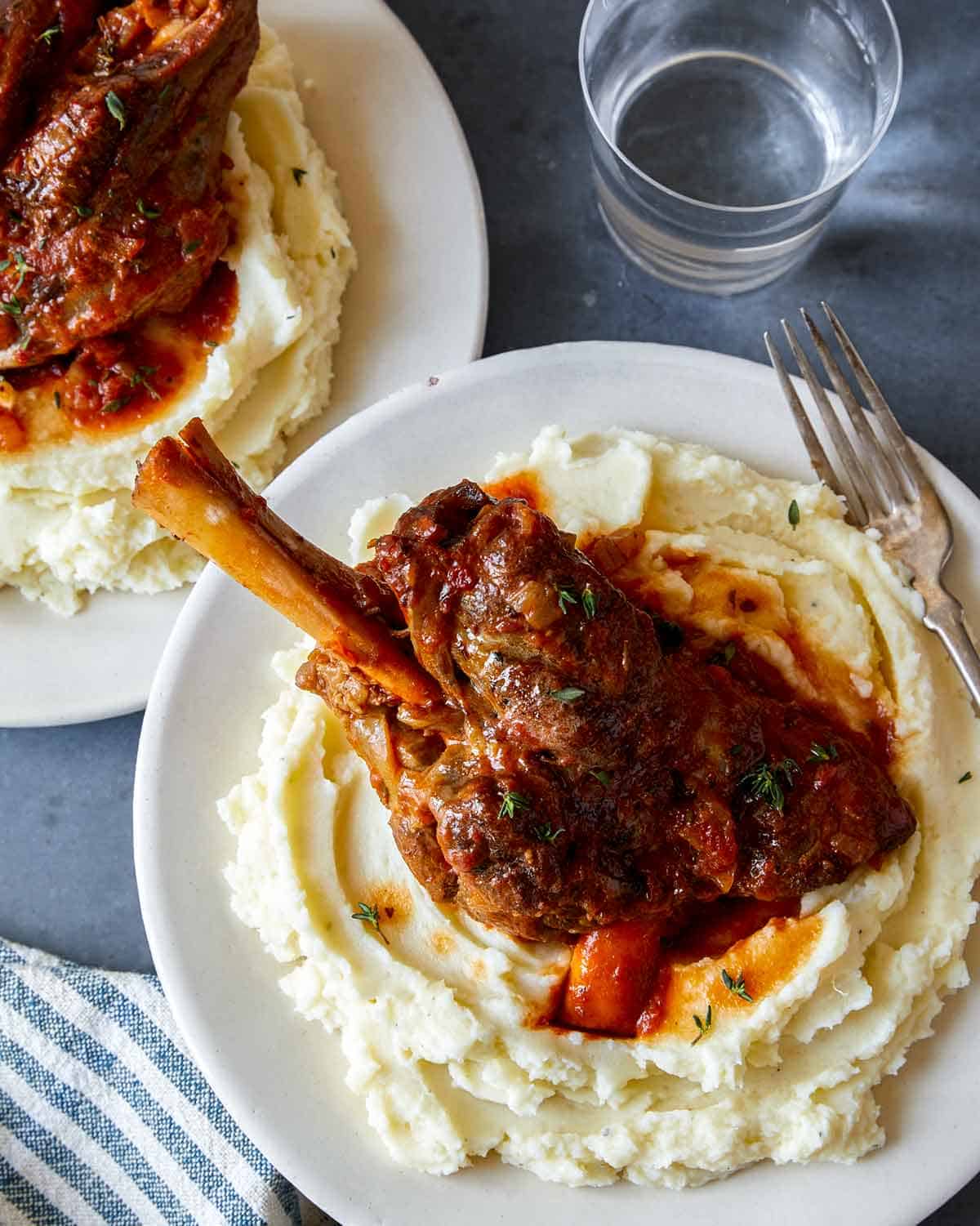 Braised lamb shanks on a plate with mashed potatoes.