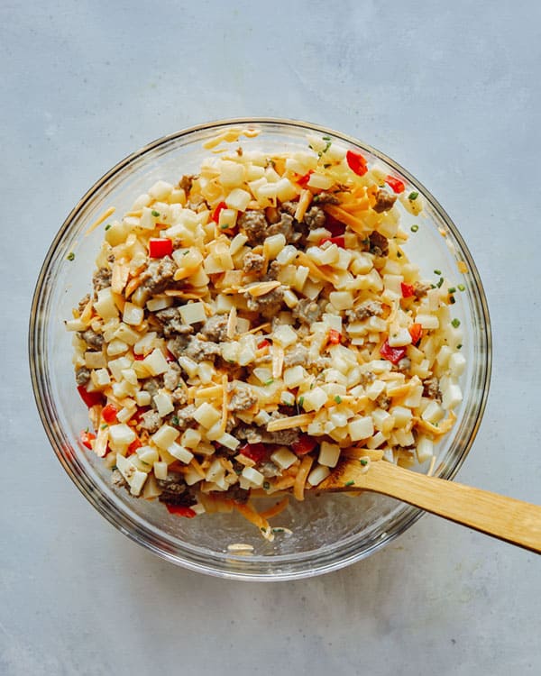 Breakfast casserole mixture in a glass bowl with a spoon in it.