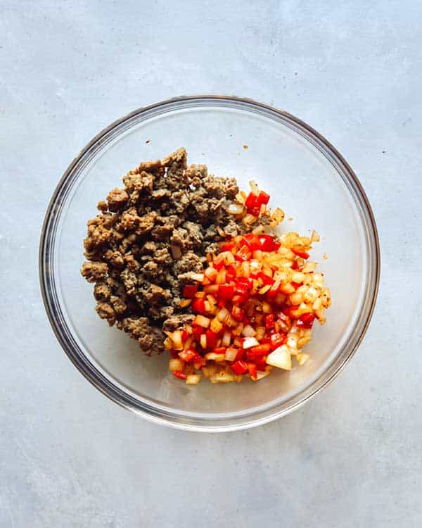 Breakfast sausage and veggies combined in a glass bowl to make breakfast casserole.