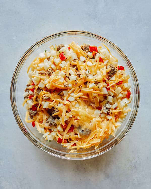Breakfast casserole mixture in a glass bowl with cheese.