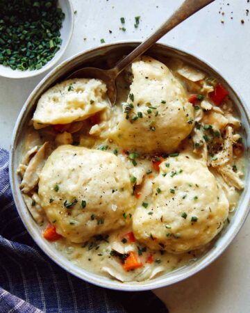 Chicken and Dumplings recipe in a bowl with a spoon taken a piece out of one of the dumplings.