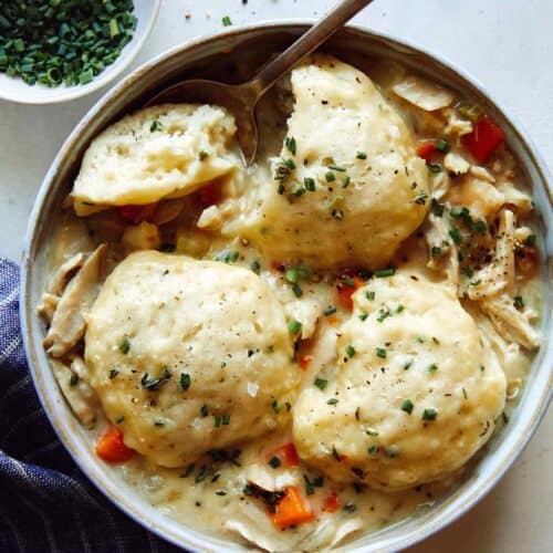 Chicken and Dumplings recipe in a bowl with a spoon taken a piece out of one of the dumplings.