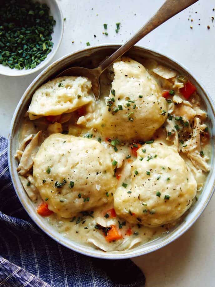 Chicken and Dumplings soup recipe in a bowl with a spoon taken a piece out of one of the dumplings.