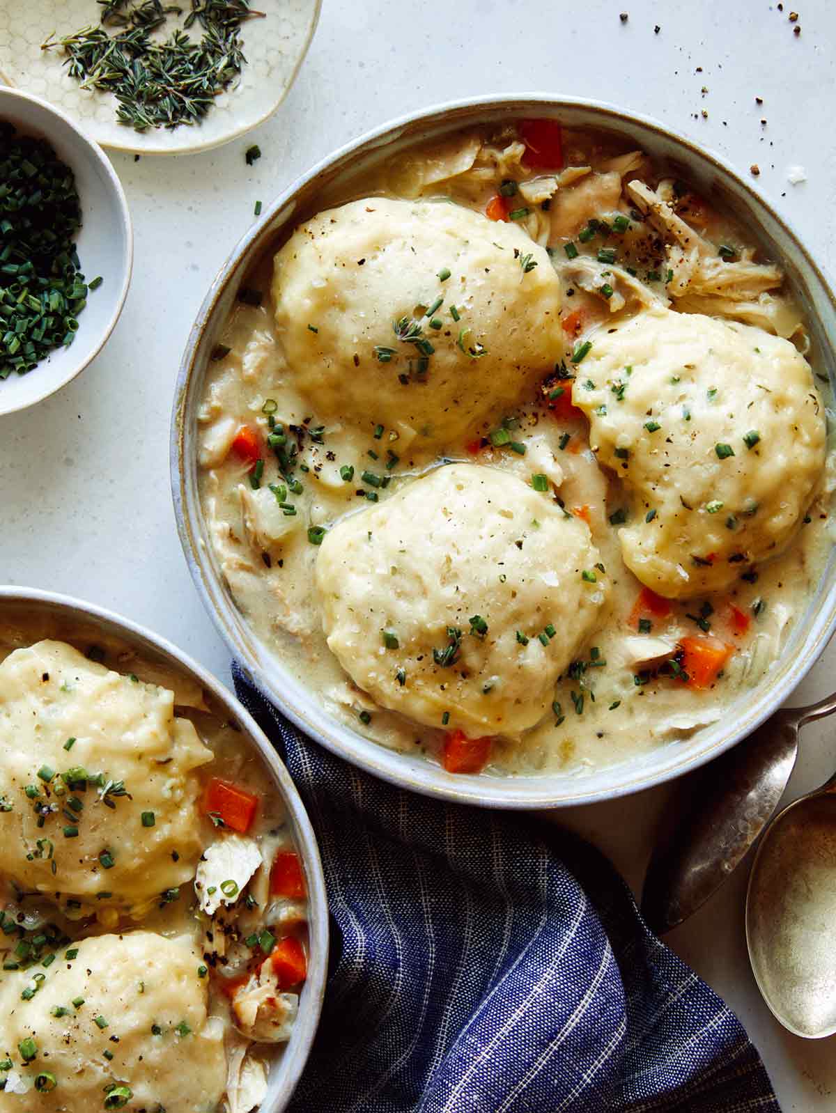 Chicken and dumplings recipe made in two bowls with garnishes on the side.