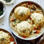 Chicken and dumplings recipe made in two bowls with garnishes on the side.