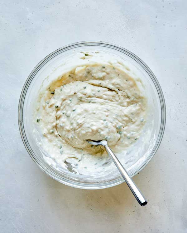 Batter for dumplings in a glass bowl with a spoon.