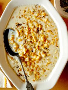 Creamed corn recipe in a serving dish with a spoon in it and fresh pepper on top.