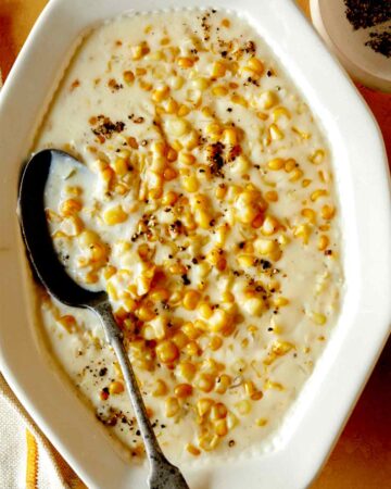 Creamed corn recipe in a serving dish with a spoon in it and fresh pepper on top.