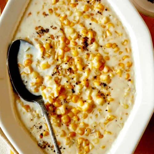 Creamed corn recipe in a serving dish with a spoon in it and fresh pepper on top.