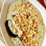 Creamed corn in a bowl with a spoon in it on a table.