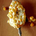 Close up on a spoon full of creamed corn on a table.