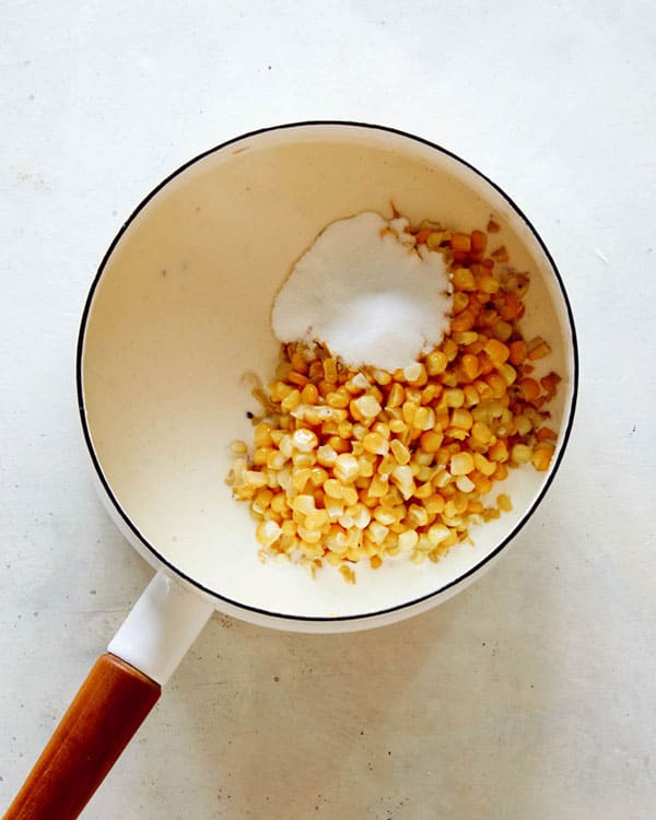 Corn added into a skillet with cream to make creamed corn.
