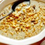 Creamed corn in a bowl with a spoon in it on a table.