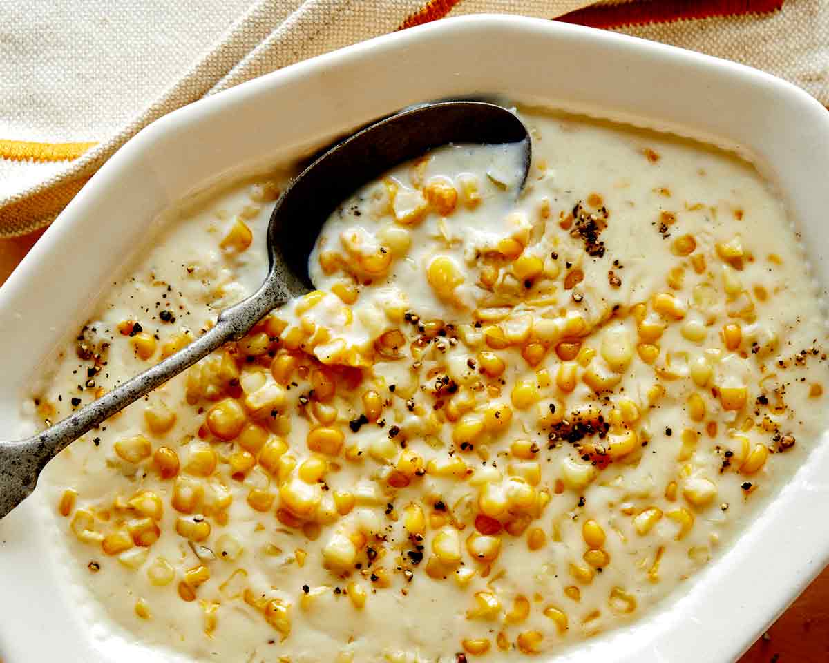 Creamed corn in a bowl close up with a spoon on it and a napkin on the side.