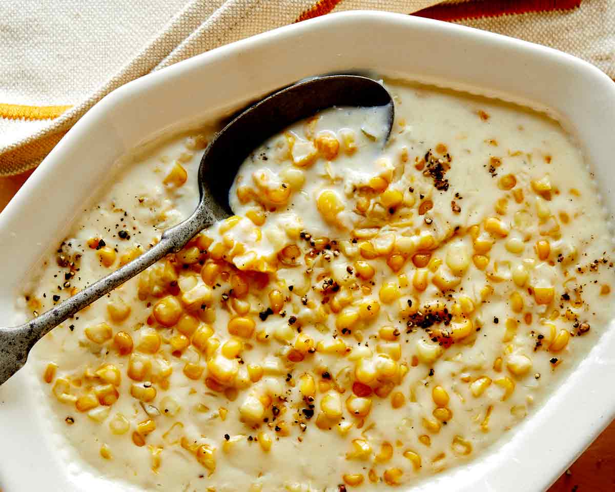 Creamed corn in a bowl close up with a spoon on it and a napkin on the side. 