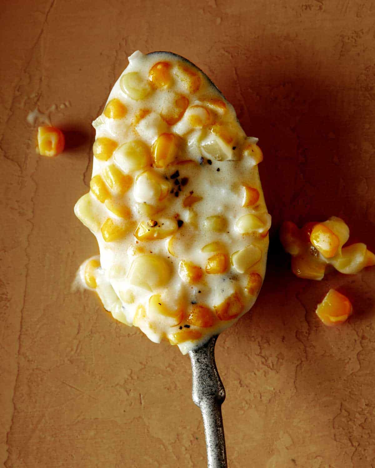 Close up on a spoon full of creamed corn on a table.