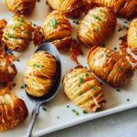 Cheesy Hasselback potatoes on a platter with a spoon.