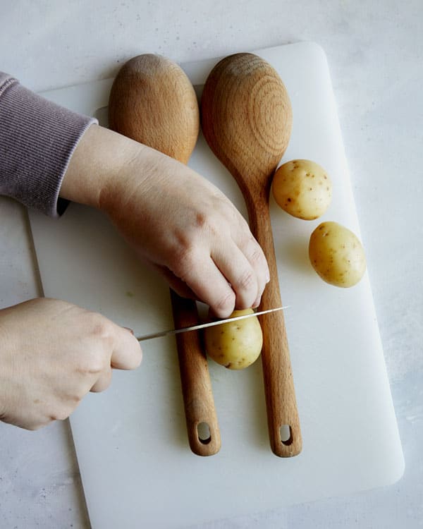 Cutting hasselback potatoes with wooden spoons.