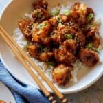 A close up of a bowl of honey garlic cauliflower over white rice with chopsticks.