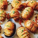 Cheesy Hasselback potatoes on a platter with a spoon.