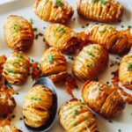 Cheesy Hasselback potatoes on a platter with a spoon.