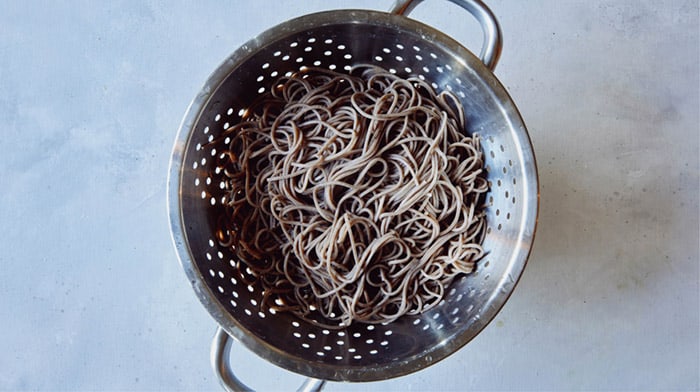 Boiled and drained soba noodles in a colander.
