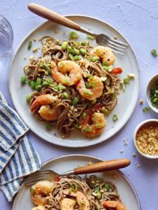 Shrimp and soba noodle recipe on two plates with sesame seeds on the side.