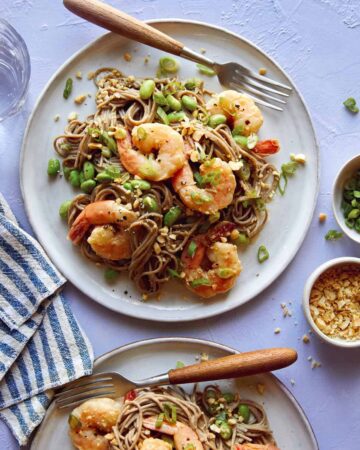 Shrimp and soba noodle recipe on two plates with sesame seeds on the side.