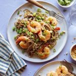 Soba noodles with shrimp on two plates with forks and garnish next to it.